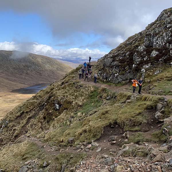 A group of people walking on a rocky path on a hill in the Peak District.