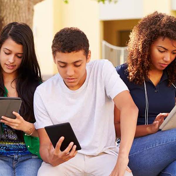 Three university students sat on a bench outside reading tablets.